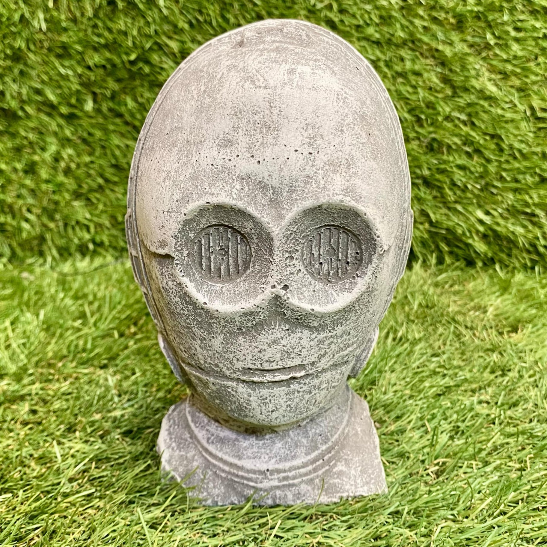 Stone sculpture of an C3 PO head on grass