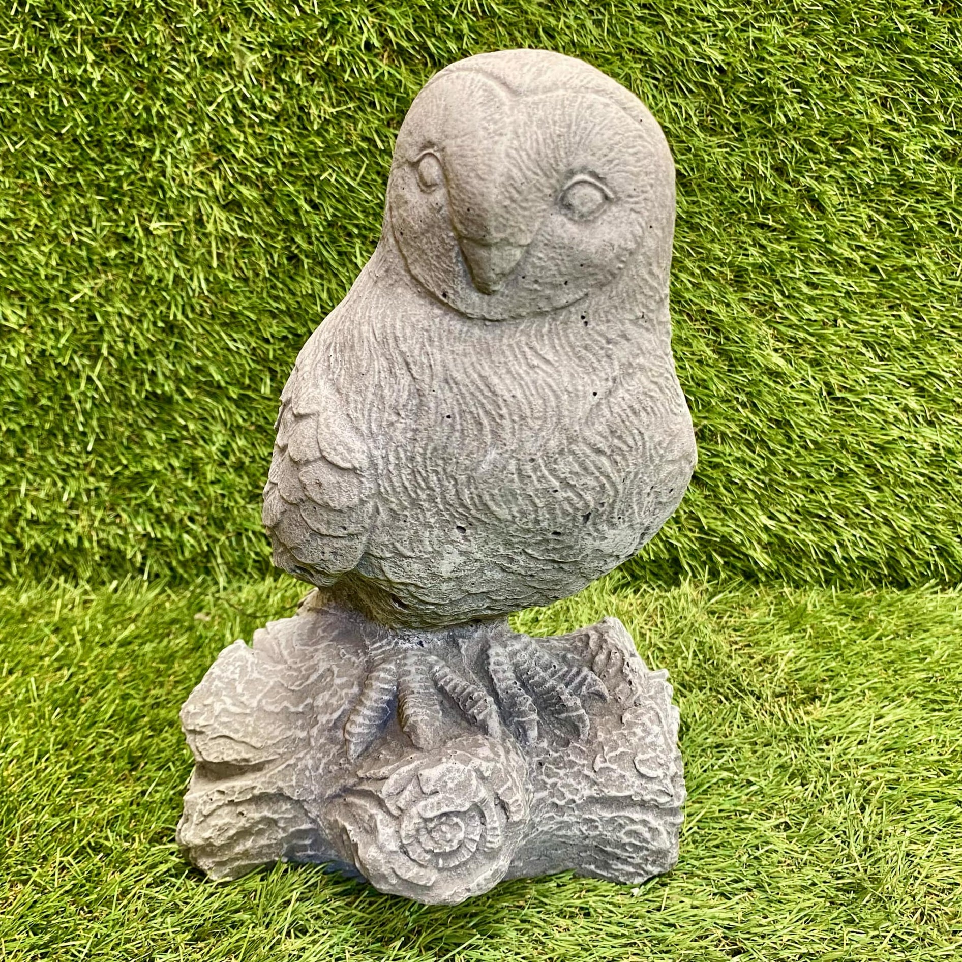 Stone owl sculpture on a log against a grassy background