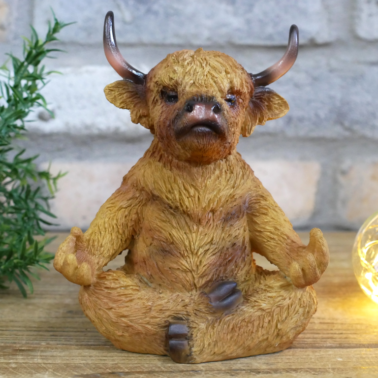 Statue of a meditating creature with horns on a wooden surface with plants and lights in the background.