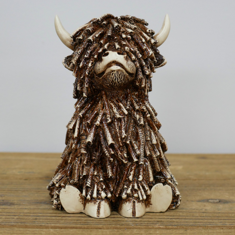 Ceramic sculpture of a highland cow with a textured brown coat on a wooden surface.